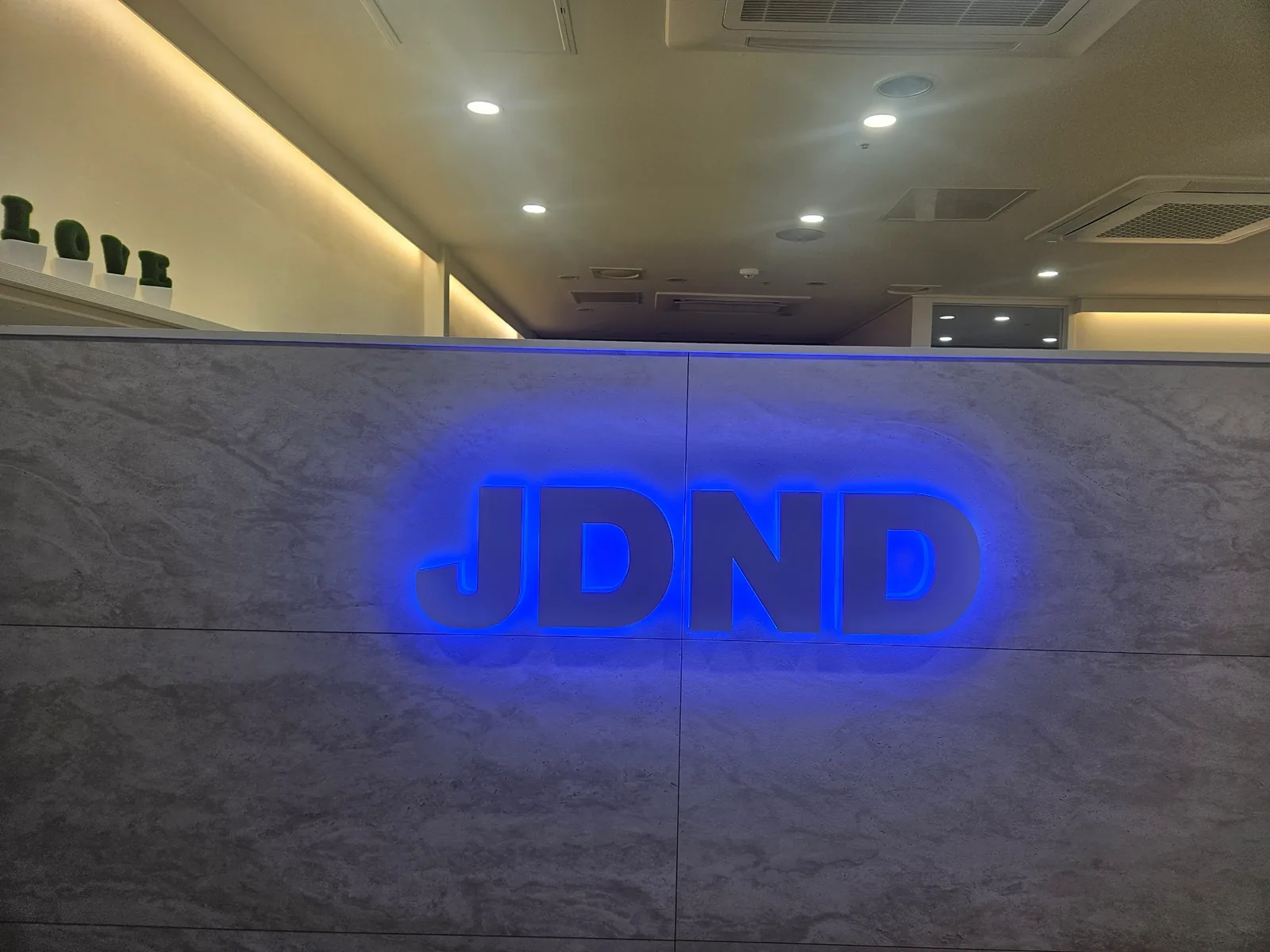 대리석 무늬 벽에 파란 조명으로 빛나는 JDND 글자